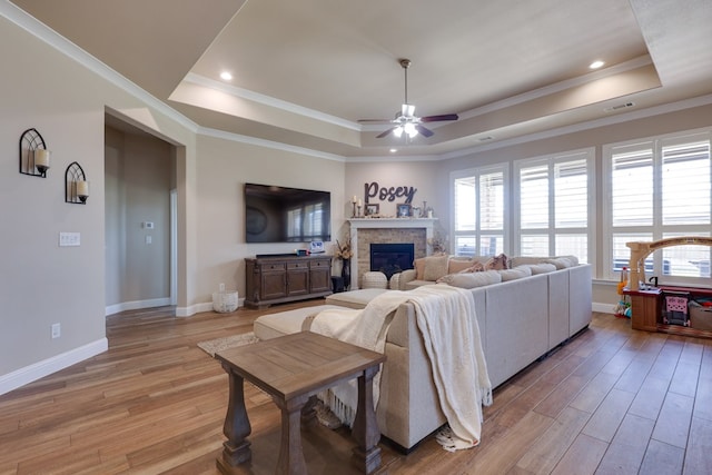 living room featuring a tray ceiling, light wood finished floors, a ceiling fan, a fireplace, and baseboards