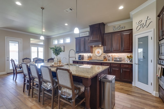 kitchen with a sink, a kitchen breakfast bar, appliances with stainless steel finishes, light wood finished floors, and light stone counters