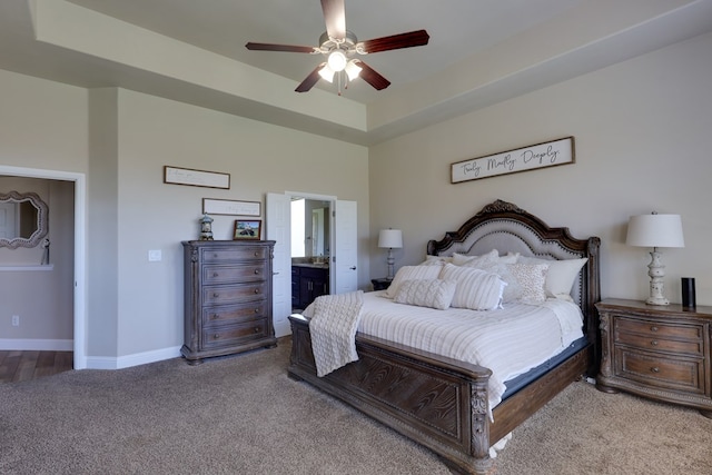 bedroom featuring carpet flooring, baseboards, a raised ceiling, a ceiling fan, and ensuite bathroom