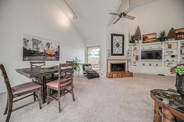 carpeted dining room featuring a tiled fireplace, ceiling fan, and high vaulted ceiling