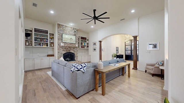 living room featuring ceiling fan, decorative columns, ornamental molding, a brick fireplace, and light wood-type flooring