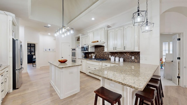 kitchen featuring stainless steel appliances, a kitchen island, white cabinets, and decorative light fixtures