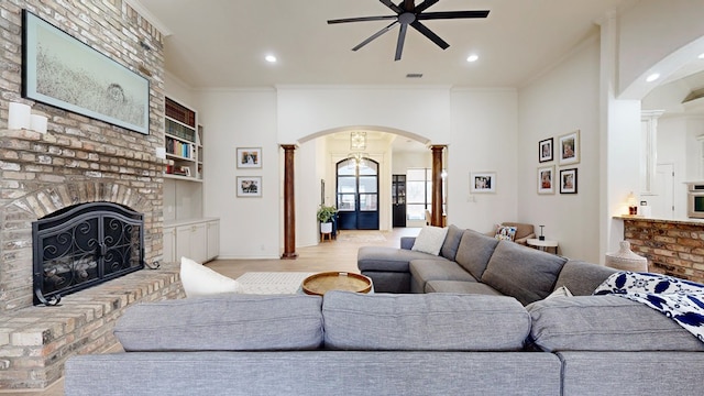 living room with crown molding, a fireplace, light wood-type flooring, and ornate columns