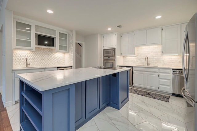 kitchen with light stone countertops, a center island, sink, white cabinets, and appliances with stainless steel finishes