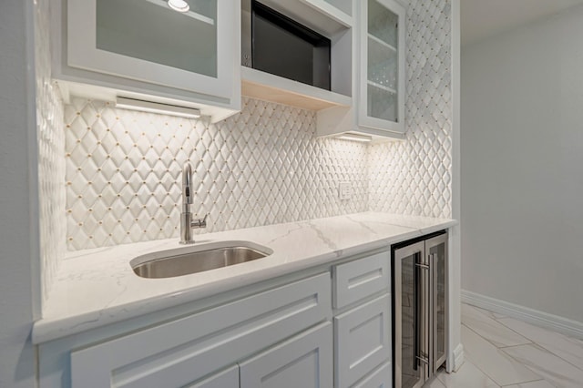 kitchen with light stone countertops, white cabinetry, sink, and beverage cooler