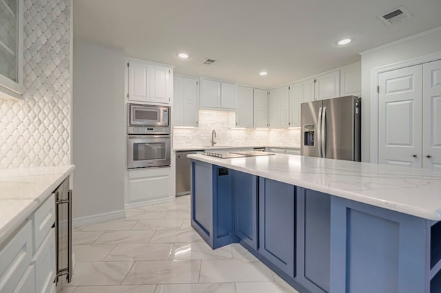 kitchen featuring backsplash, blue cabinets, light stone countertops, appliances with stainless steel finishes, and white cabinetry