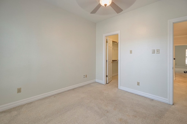 unfurnished bedroom featuring a closet, a walk in closet, light colored carpet, and ceiling fan