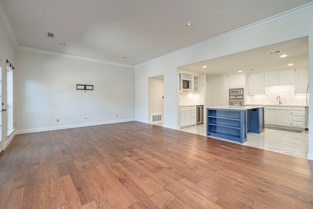 unfurnished living room featuring light hardwood / wood-style floors, ornamental molding, sink, and beverage cooler