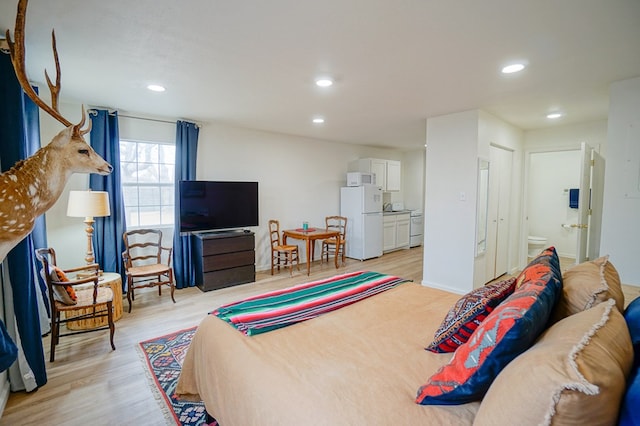 bedroom featuring white fridge, light wood-type flooring, and ensuite bath