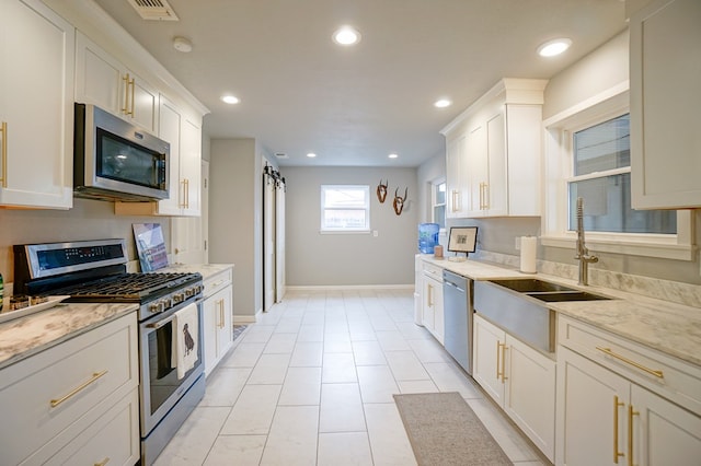 kitchen with white cabinetry, stainless steel appliances, light stone countertops, and sink