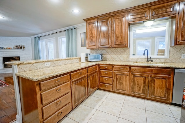 kitchen featuring light stone countertops, sink, a brick fireplace, backsplash, and kitchen peninsula