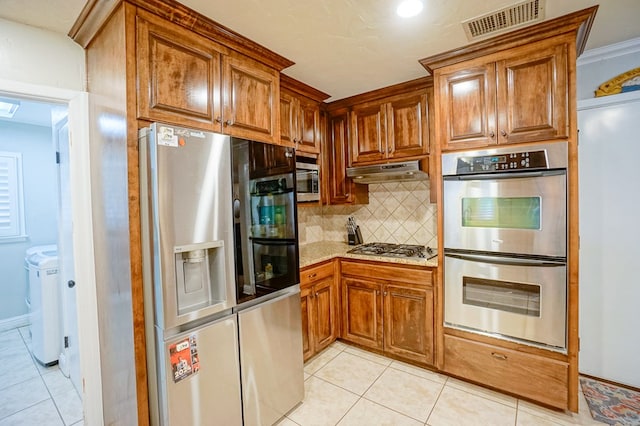 kitchen with decorative backsplash, washing machine and dryer, light tile patterned floors, and stainless steel appliances