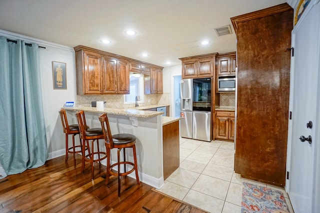 kitchen with kitchen peninsula, appliances with stainless steel finishes, light stone counters, a breakfast bar, and light hardwood / wood-style floors