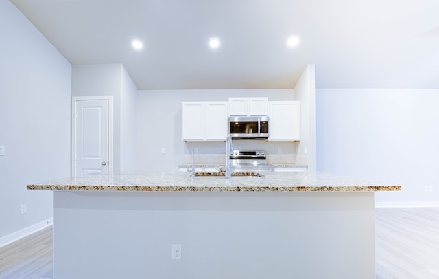 307 Pioneer Cir, Midland, TX 79705 - kitchen with stainless steel appliances, light wood-style floors, a center island with sink, light stone counters, and white cabinets