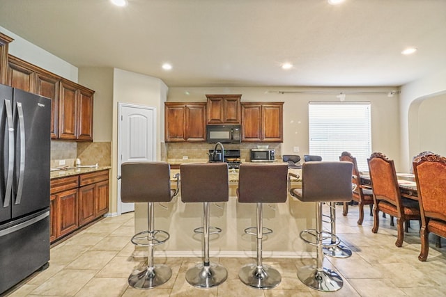 kitchen featuring a kitchen bar, appliances with stainless steel finishes, a center island with sink, and decorative backsplash