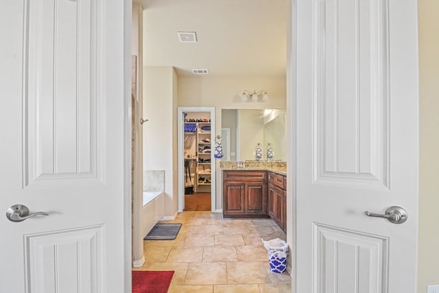 bathroom with tile patterned flooring, vanity, and a relaxing tiled tub