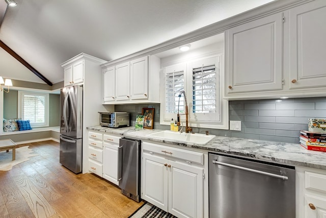 kitchen featuring vaulted ceiling, white cabinetry, sink, stainless steel appliances, and light wood-type flooring