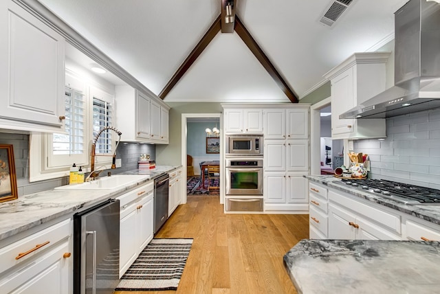 kitchen with white cabinetry, stainless steel appliances, sink, and wall chimney range hood