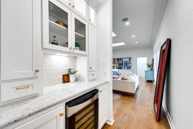 bar featuring white cabinetry, light stone counters, ornamental molding, and beverage cooler