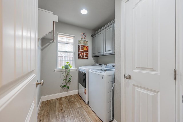 clothes washing area featuring washer and clothes dryer, cabinet space, light wood-style floors, and baseboards