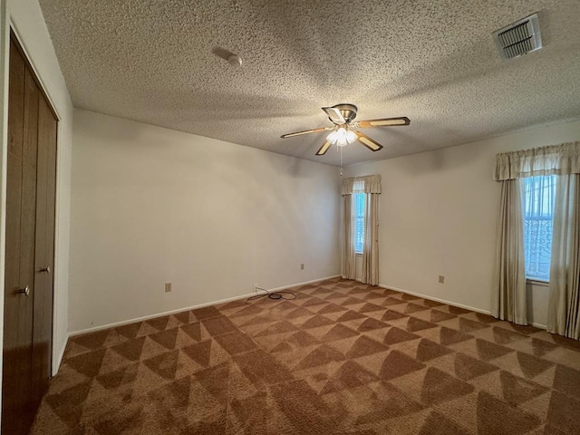 spare room with ceiling fan, dark carpet, and a textured ceiling