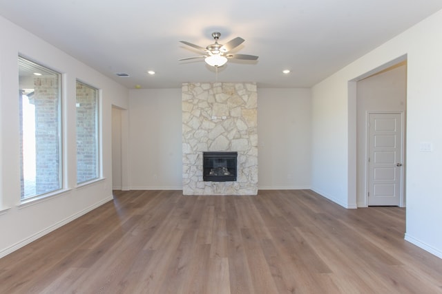 unfurnished living room featuring a stone fireplace, light hardwood / wood-style floors, and ceiling fan