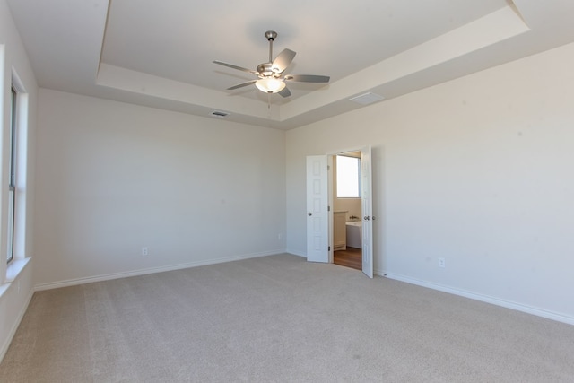 unfurnished room featuring light carpet, a tray ceiling, and ceiling fan