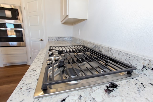 room details featuring white cabinetry, light stone countertops, dark wood-type flooring, and stainless steel appliances