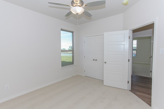 unfurnished bedroom with ceiling fan, a closet, light colored carpet, and multiple windows