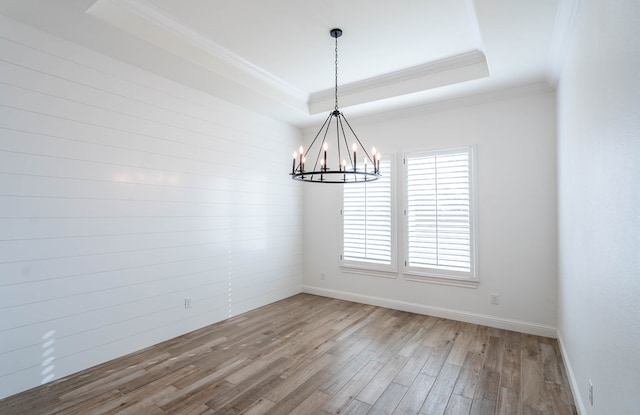 spare room with wood-type flooring, a tray ceiling, ornamental molding, and a notable chandelier