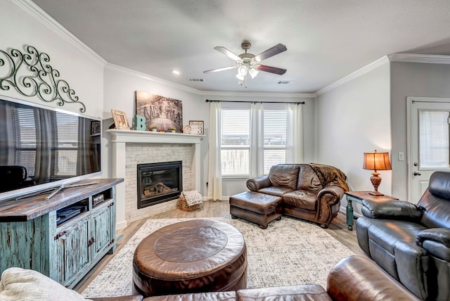 living room featuring ceiling fan, light wood-type flooring, a fireplace, and ornamental molding