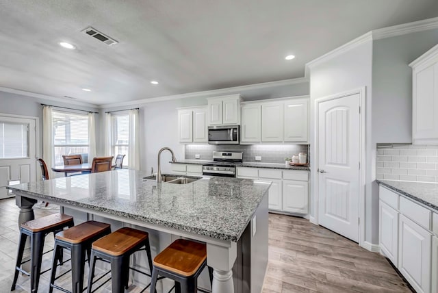 kitchen with sink, ornamental molding, stainless steel appliances, and an island with sink