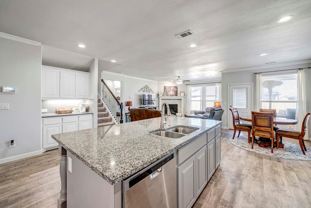 kitchen featuring white cabinetry, dishwasher, sink, a kitchen island with sink, and light wood-type flooring