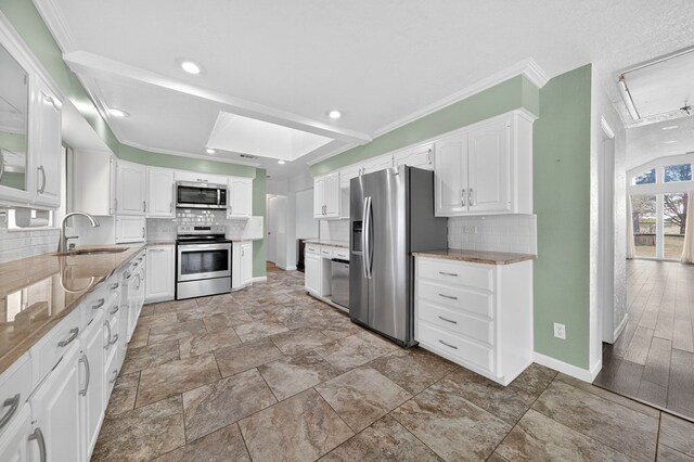 4715 N County Rd 1125, Midland, TX 79705 - kitchen featuring appliances with stainless steel finishes, backsplash, white cabinetry, light stone countertops, and ornamental molding