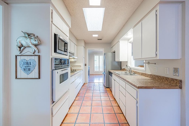 kitchen featuring a skylight, sink, white cabinets, light tile patterned floors, and stainless steel appliances