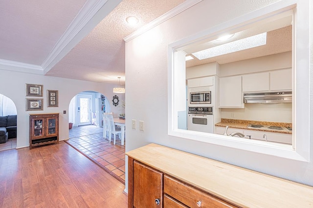 kitchen with white appliances, wood-type flooring, ornamental molding, white cabinets, and a textured ceiling