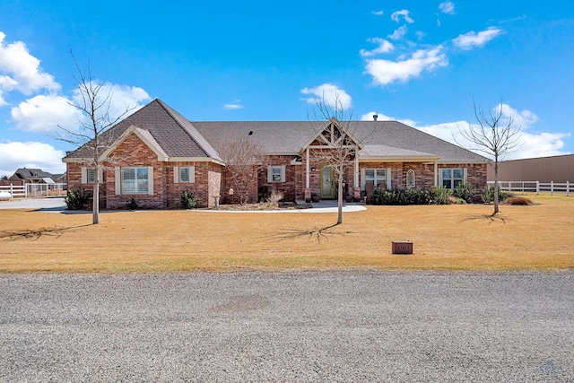 view of front of property featuring brick siding, fence, a front lawn, and roof with shingles