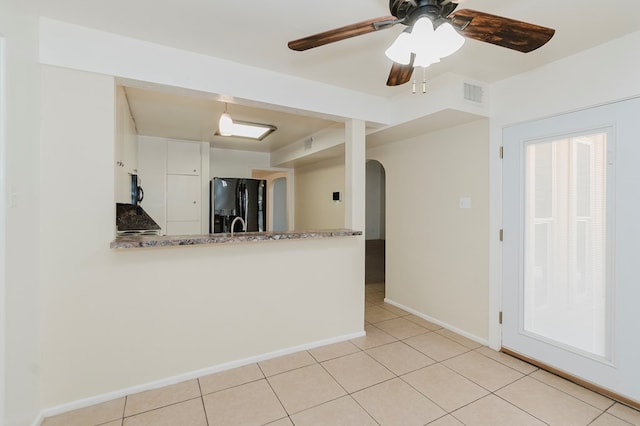 spare room with light tile patterned floors, arched walkways, a ceiling fan, visible vents, and baseboards