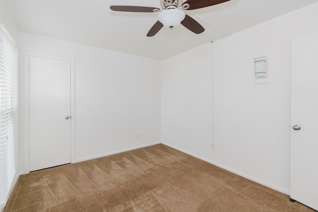 carpeted spare room featuring baseboards and a ceiling fan