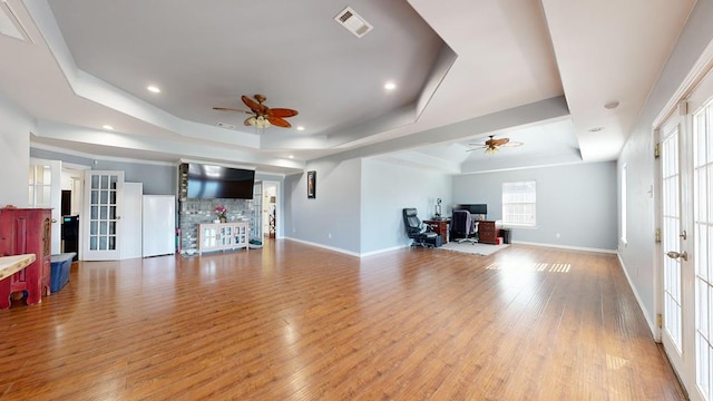 living room featuring a tray ceiling, ceiling fan, a healthy amount of sunlight, and light wood-type flooring