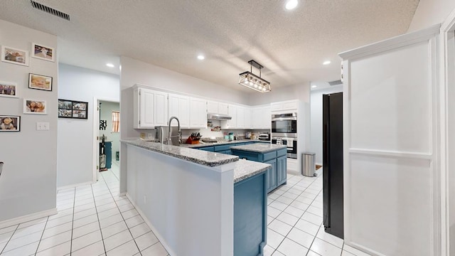 kitchen featuring blue cabinets, light tile patterned floors, a textured ceiling, double oven, and white cabinetry