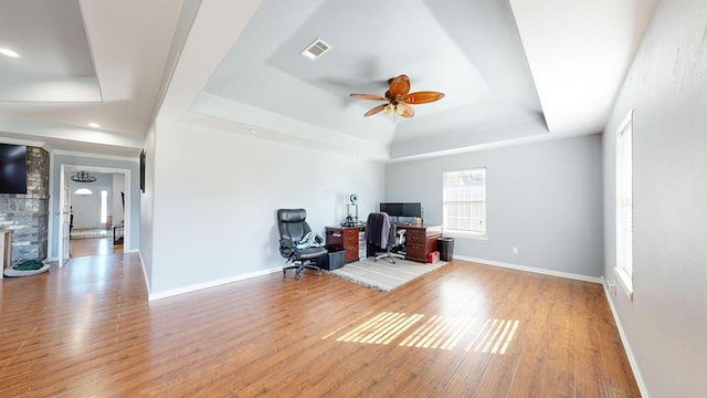 office space featuring a raised ceiling, ceiling fan, and light wood-type flooring