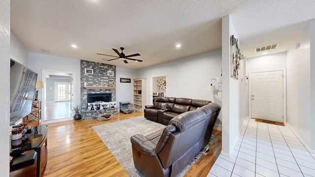 living room featuring ceiling fan, a large fireplace, a textured ceiling, and light wood-type flooring