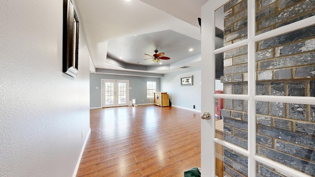 living room featuring ceiling fan, a raised ceiling, wood-type flooring, and french doors