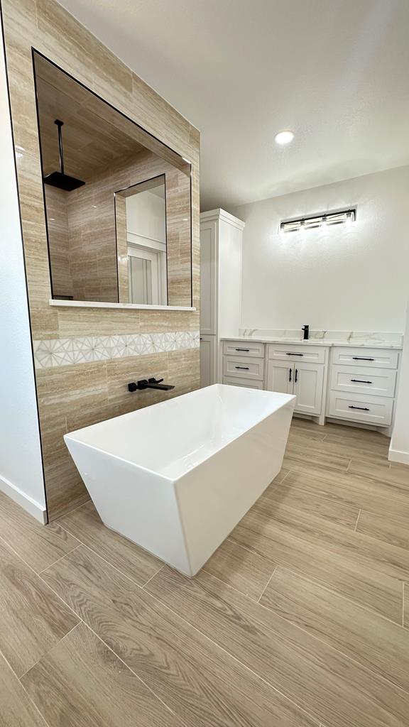 2118 S County Rd 1059, Midland, TX 79706 - bathroom featuring a soaking tub, baseboards, tile walls, vanity, and recessed lighting