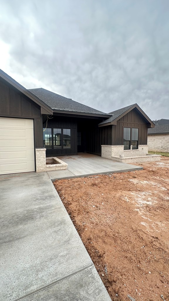 view of side of home featuring brick siding, board and batten siding, an attached garage, and roof with shingles