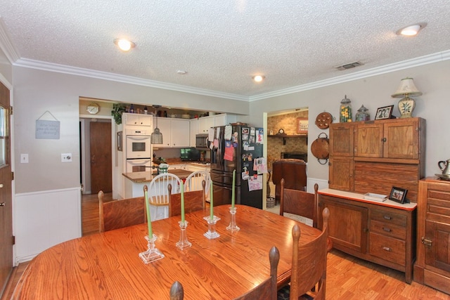 702 Capri Ct, Big Spring, TX 79720 - dining area with ornamental molding, a textured ceiling, light wood finished floors, and a large fireplace