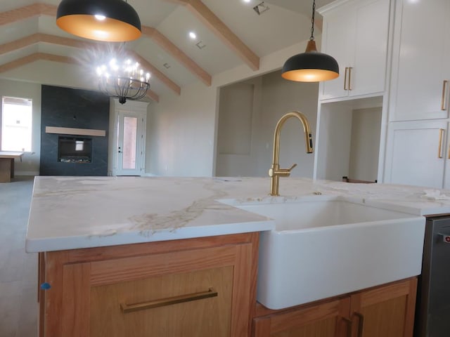 kitchen featuring a sink, light stone counters, pendant lighting, open floor plan, and vaulted ceiling with beams