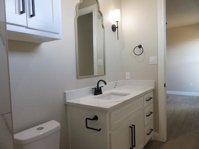 half bath with vanity, toilet, baseboards, and wood finished floors