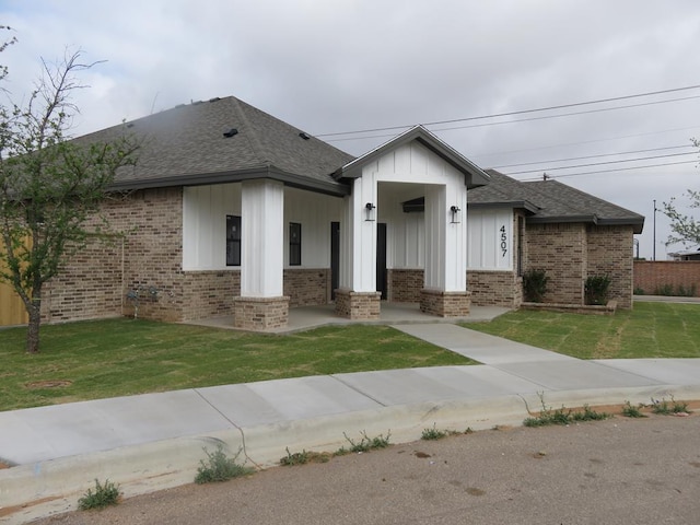 view of front of home with a shingled roof, brick siding, and a front lawn